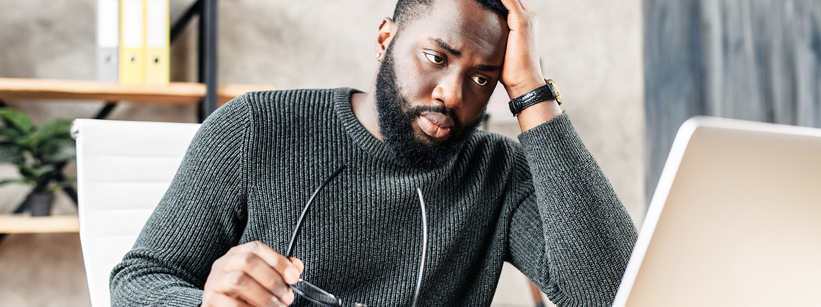 a man holding his glasses while staring at his laptop screen.