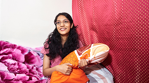 Sabiha sitting on her bed holding a pillow in her lap