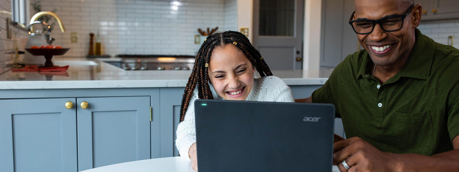 An adult and a young person laughing and smiling at a computer screen.