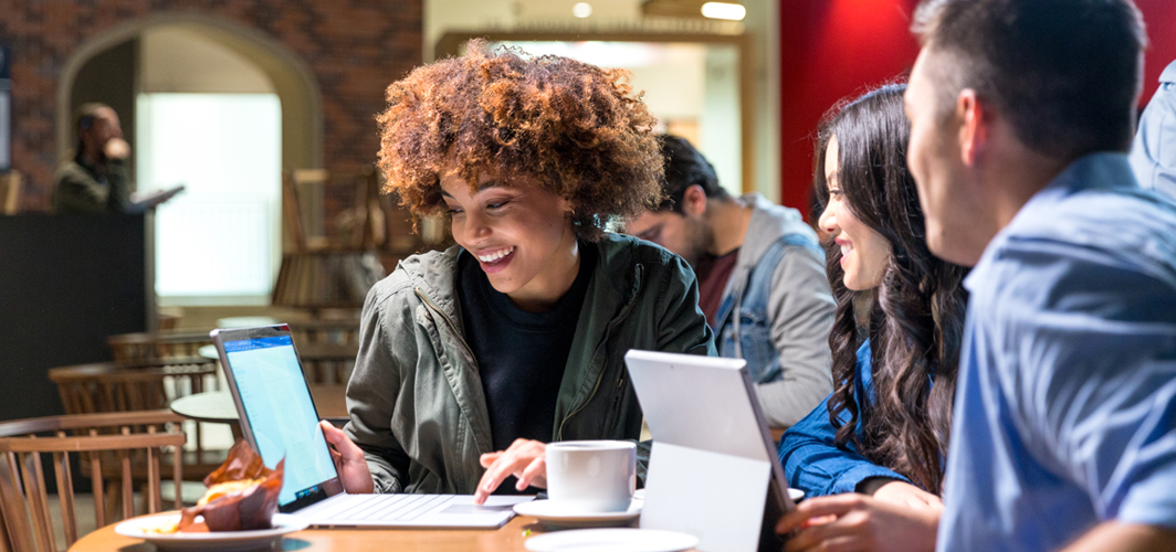 A group of people at a coffee shop sharing information using a tablet.