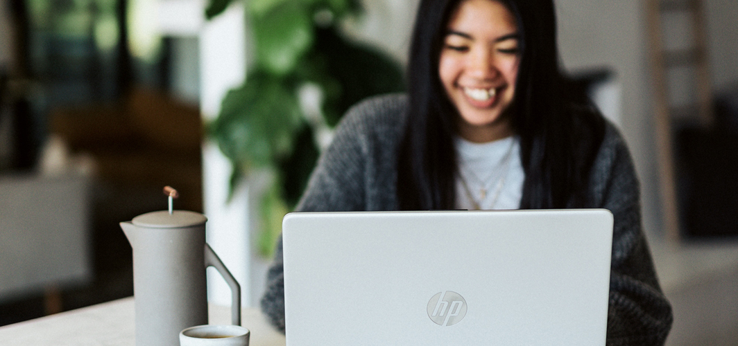 A young person smiling at a laptop.
