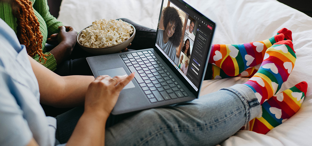Two people sitting on a couch with popcorn on a video chat with friends.
