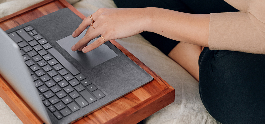 A top down view of someone using a trackpad on a laptop atop a small desk.