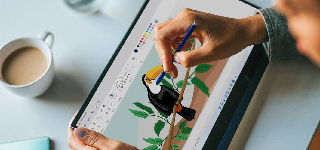 A top down view of someone using a tablet and stylus to illustrate a toucan.