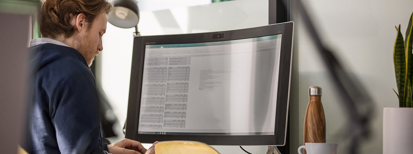 A man working at a desk with a widescreen curved monitor.