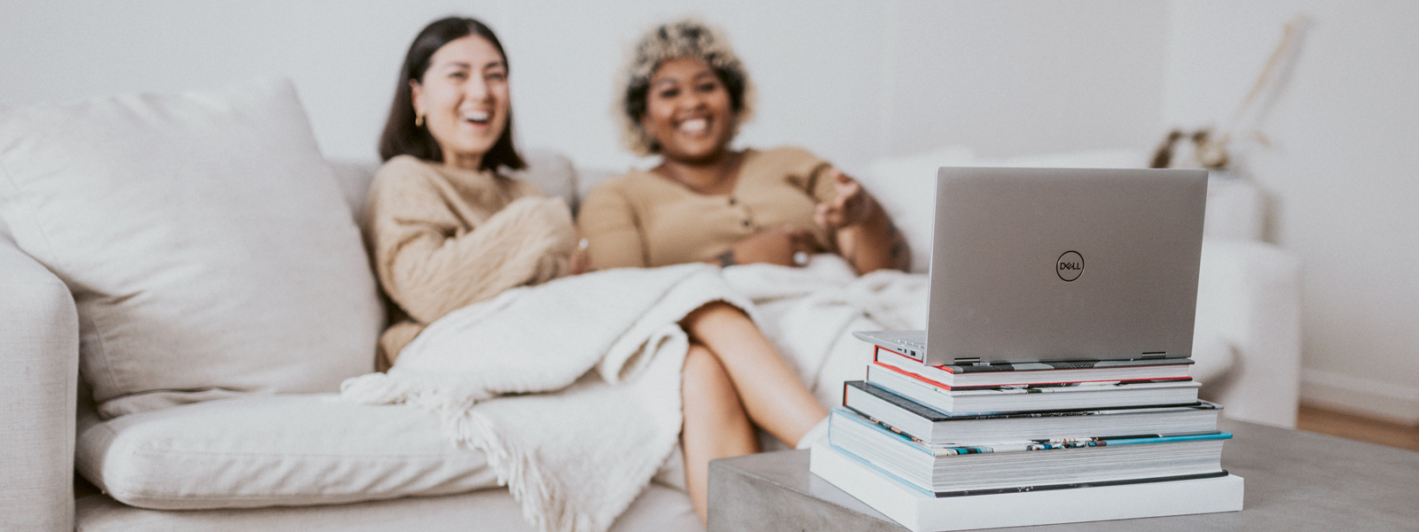 Two people sitting on a couch laughing watching a show on a laptop atop a stack of college textbooks.