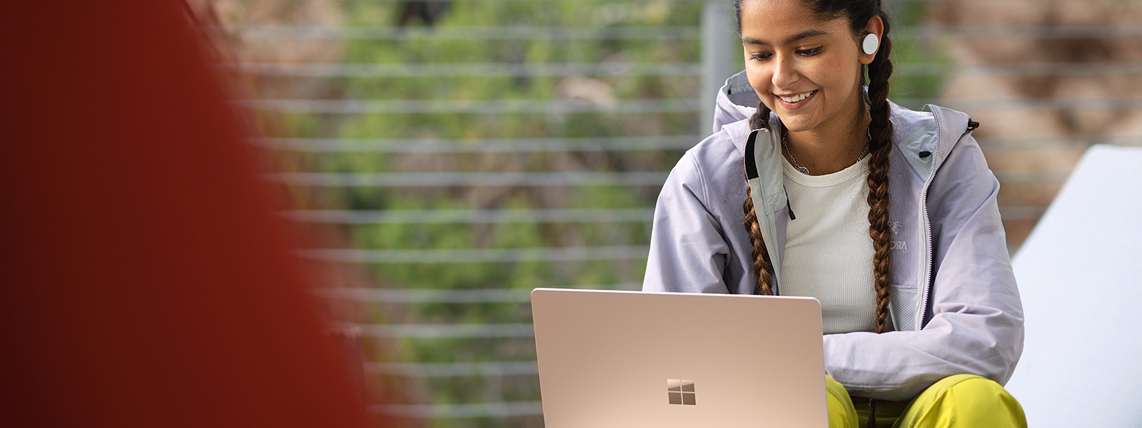A young woman with earbuds in smiling while looking at a laptop.
