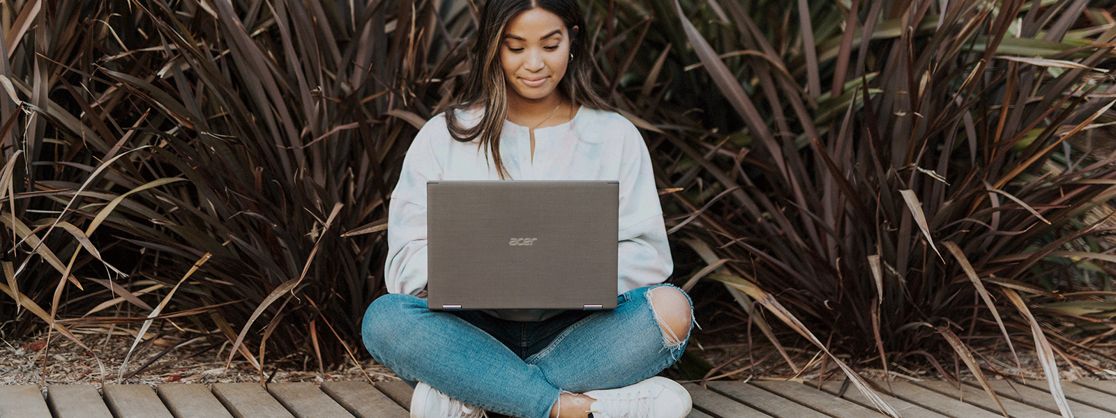 Someone sitting outside on a wooden path studying on a laptop.