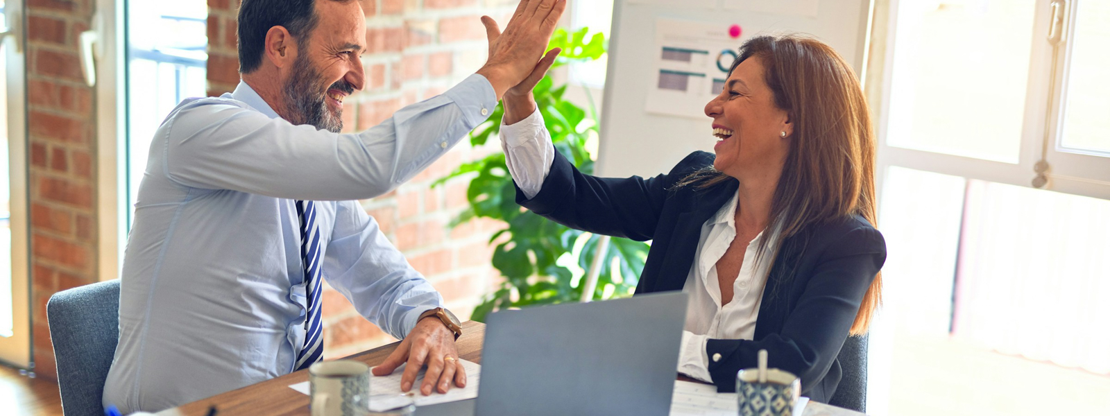 A man and woman high fiving at a desk