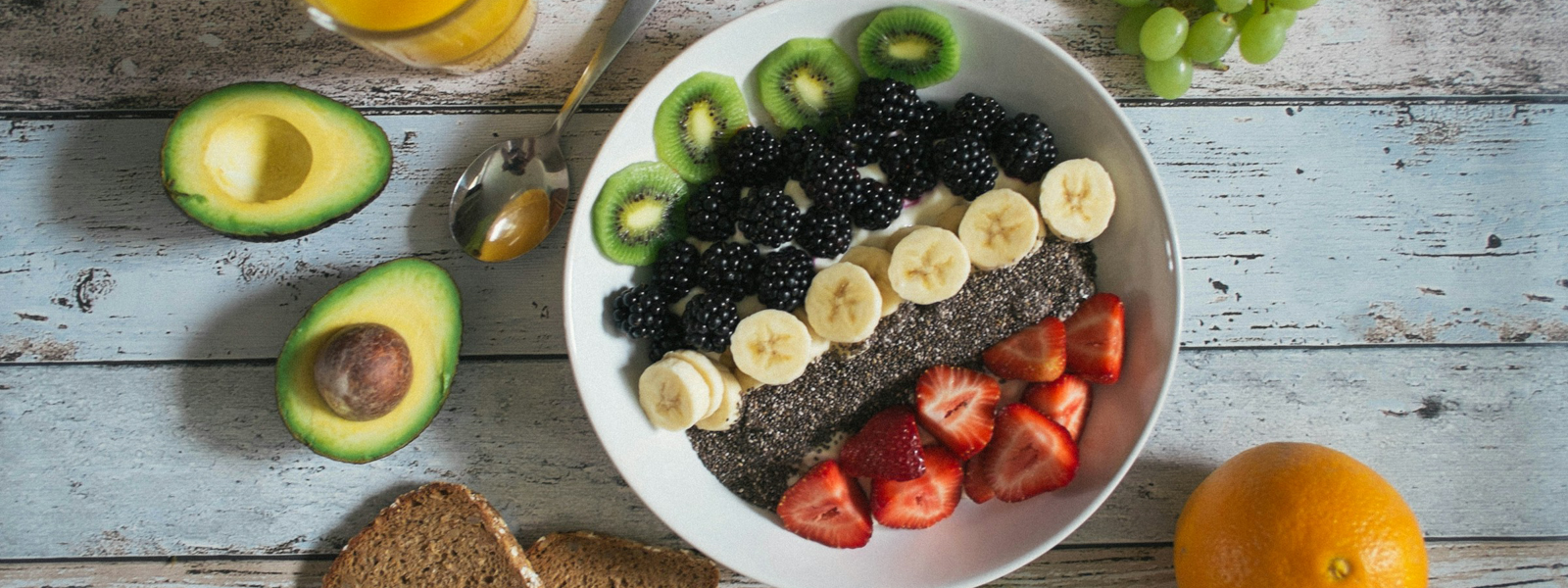 Fruit on a white plate next to avocados, toast, and orange juice