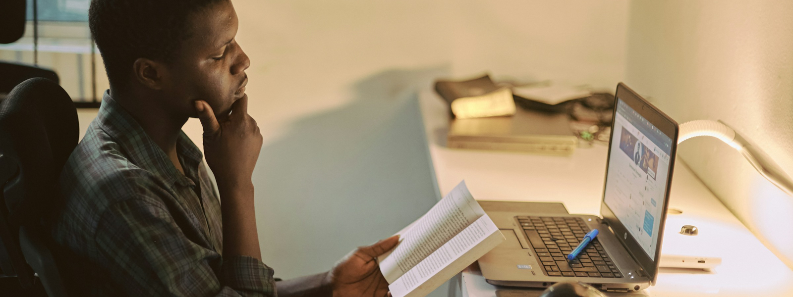 Man reading a book in front of his computer
