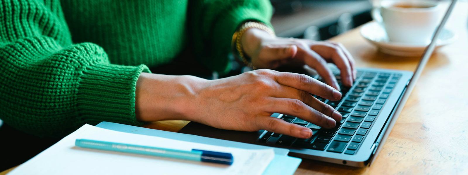 Person wearing a green sweater typing on a laptop