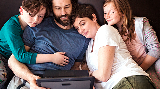 a family of four sitting together and huddled around a laptop