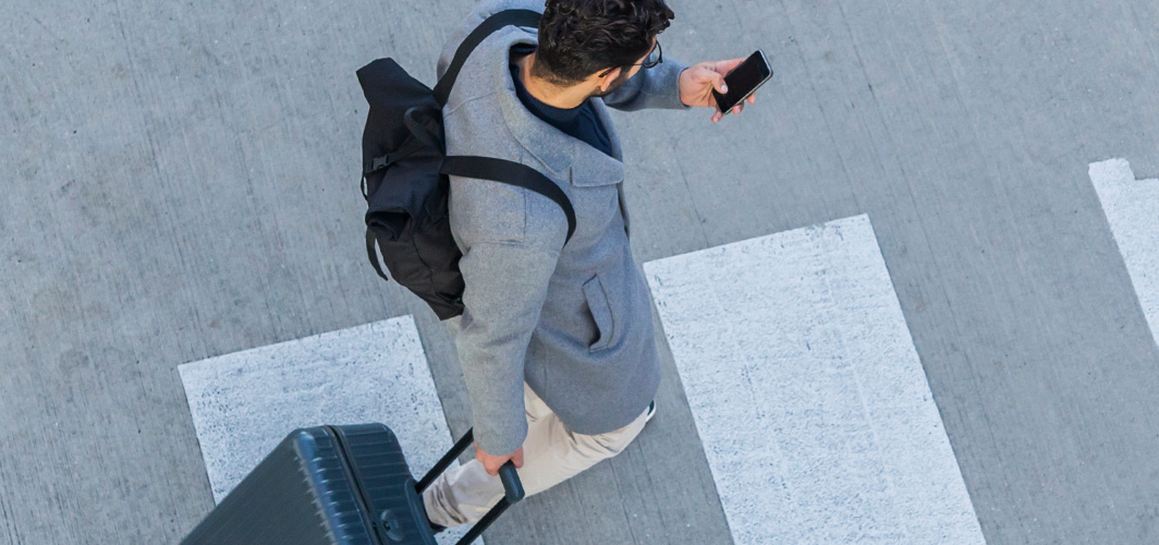 Businessman with baggage crossing the street while looking at cell phone.