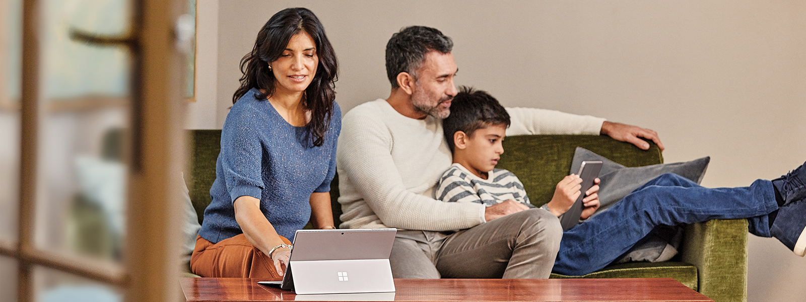 Family at home in sofa with mobile professional mother on Surface Pro, father and son on Surface Go.
