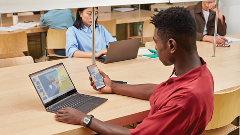 Young adult students inside library cross device experiences on phone and laptop using PowerPoint. Back to school. Lenovo Yoga C630