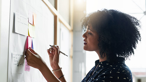 a young female designer working in her office looking at diferent colored sticky notes on a board