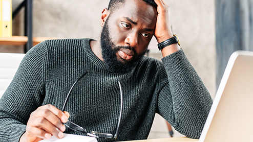 a man holding his glasses while staring at his laptop screen.