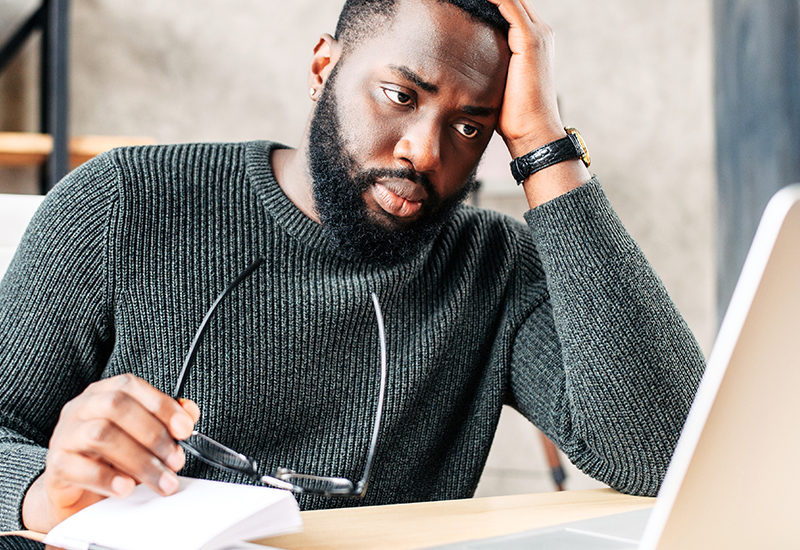 a man holding his glasses while staring at his laptop screen.